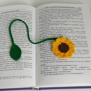 May include: A crocheted sunflower bookmark with a green stem and leaves. The bookmark is laying on top of an open book with text about accounting.