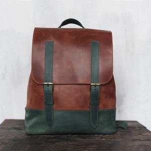 May include: A brown leather backpack with green leather straps and buckles. The backpack has a flap closure and a top handle.
