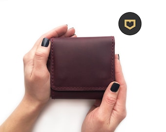 May include: A burgundy leather wallet with a stitched edge, held in two hands.