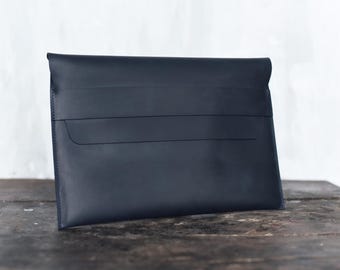 May include: A navy blue leather document case or portfolio. The case has a simple design with three horizontal lines across the front. The case is sitting on a weathered wooden surface.
