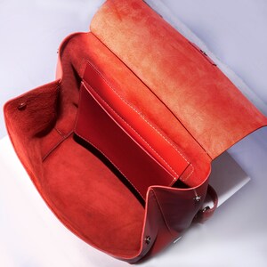 May include: A red leather handbag with a flap top and a zipper closure. The bag is open and the inside is lined with a red fabric.