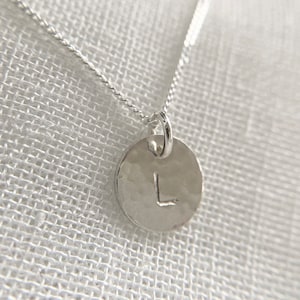 May include: A silver necklace with a hammered silver pendant featuring the letter L.