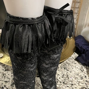 May include: Black lace stockings with a black fringe trim at the top. The fringe is tied with a bow.