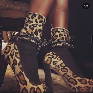 May include: A pair of black heeled shoes with leopard print fabric. The shoes have a black fabric cuff with a white trim and a bow.