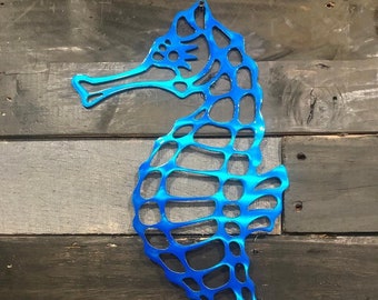 Puede incluir: Una decoración de pared de metal azul en forma de caballito de mar con un diseño recortado. El caballito de mar está hecho de metal y tiene un acabado brillante y metálico.