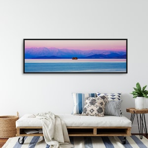 May include: A panoramic photograph of a mountain range in the distance, with a small island in the middle of a body of water. The sky is a vibrant pink and purple, and the water is a deep blue.
