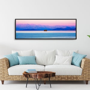 May include: A panoramic photograph of a mountain range with a small island in the middle of a lake. The sky is a vibrant pink and purple, and the water is a deep blue. The image is framed in a black frame.
