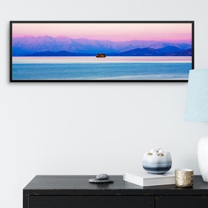 May include: A panoramic photograph of a mountain range with a pink and purple sky at sunset. A small island with trees is in the middle of a calm lake in the foreground.