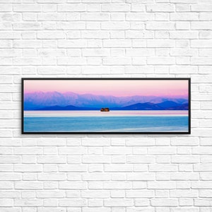 May include: A panoramic view of a small island with trees in a body of water with a mountain range in the background. The sky is a gradient of pink and blue.