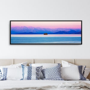 May include: A panoramic photograph of a mountain range in the distance, with a small island in the foreground. The sky is a vibrant pink and purple, reflecting in the calm water.
