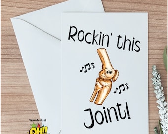 May include: A white greeting card with a cartoon drawing of a knee joint with a smiling face and musical notes. The text on the card reads "Rockin' this Joint!"