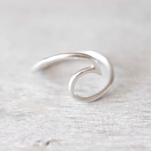 May include: A silver wave ring. The ring is made from a single piece of metal that is bent into the shape of a wave.