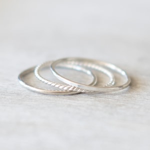 May include: Three silver stacking rings. The top ring has a twisted design, the middle ring is plain, and the bottom ring is plain.