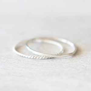 May include: Two silver rings, one with a twisted design, stacked on top of each other.