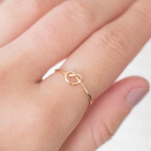 Peut inclure: Une bague en or en forme de nœud sur un doigt.