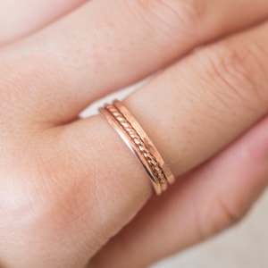 Peut inclure: Trois fines bagues en or rose empilées sur un doigt. Les bagues sont de largeurs différentes et ont un design simple et minimaliste.