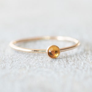 Puede incluir: Un delicado anillo de oro con una pequeña piedra preciosa redonda de color naranja.
