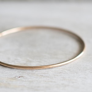 May include: A simple gold bangle bracelet. The bracelet is thin and has a smooth, polished finish.