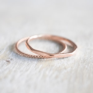 May include: Two rose gold rings, one with a hammered finish and the other with a twisted rope design.