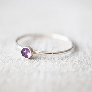 May include: A delicate silver ring with a small, round, purple amethyst gemstone.