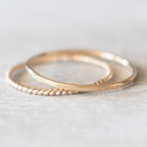 May include: Two gold rings, one with a smooth finish and the other with a twisted design, are stacked on top of each other.