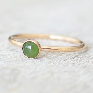 May include: A simple gold band ring with a green gemstone set in the centre.