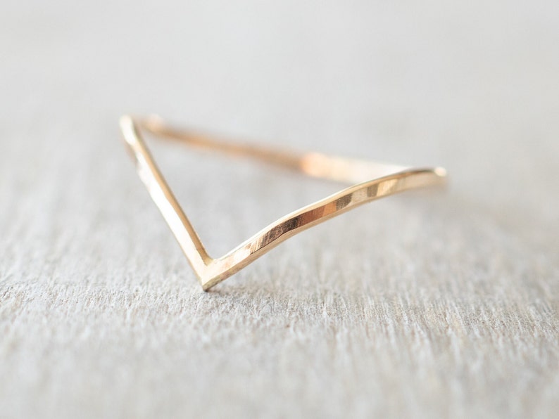 Puede incluir: Un anillo de banda de oro simple con un dise&ntilde;o en forma de V. El anillo est&aacute; hecho de metal martillado, lo que le da un aspecto texturizado.