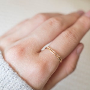 Op de afbeelding: Een close-up van een hand met twee dunne gouden ringen. De ringen zijn simpel en delicaat, met &eacute;&eacute;n ring met een textuur.