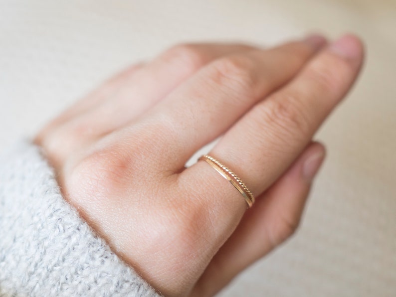 Op de afbeelding: Een close-up van een hand met twee dunne gouden ringen. De ringen zijn simpel en delicaat, met &eacute;&eacute;n ring met een textuur.