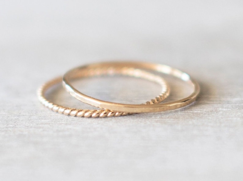 Op de afbeelding: Twee gouden ringen, een met een gladde afwerking en de andere met een gedraaid ontwerp, liggen op elkaar.