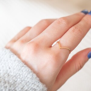 Puede incluir: Un anillo de color dorado en forma de V en un dedo. El anillo es fino y delicado.
