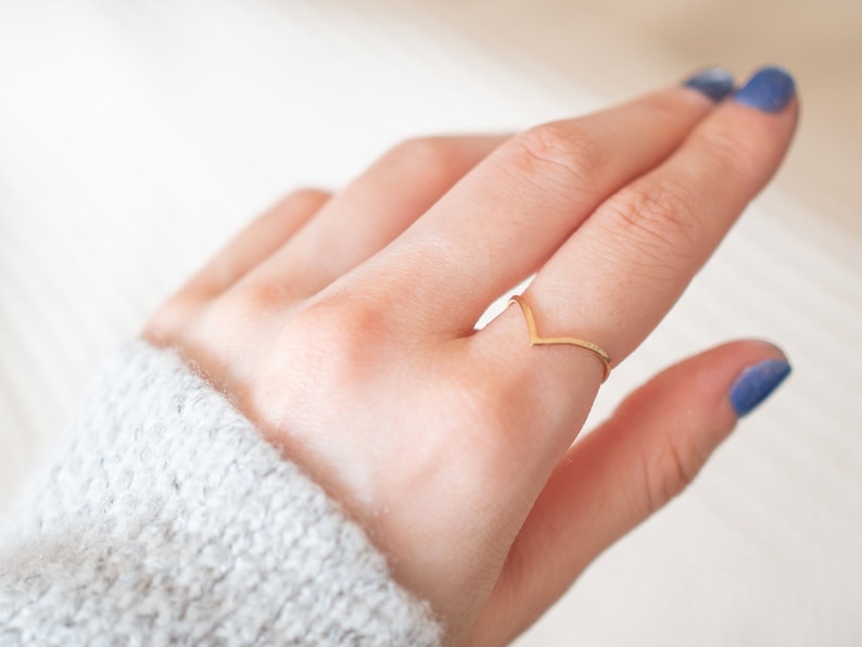 Puede incluir: Un anillo de color dorado en forma de V en un dedo. El anillo es fino y delicado.
