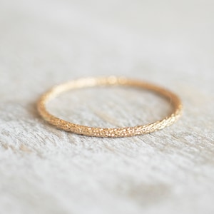 May include: A simple gold band ring with a textured surface.