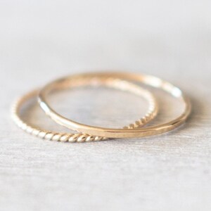 Op de afbeelding: Twee gouden ringen, een met een gladde afwerking en de andere met een gedraaid ontwerp, liggen op elkaar.