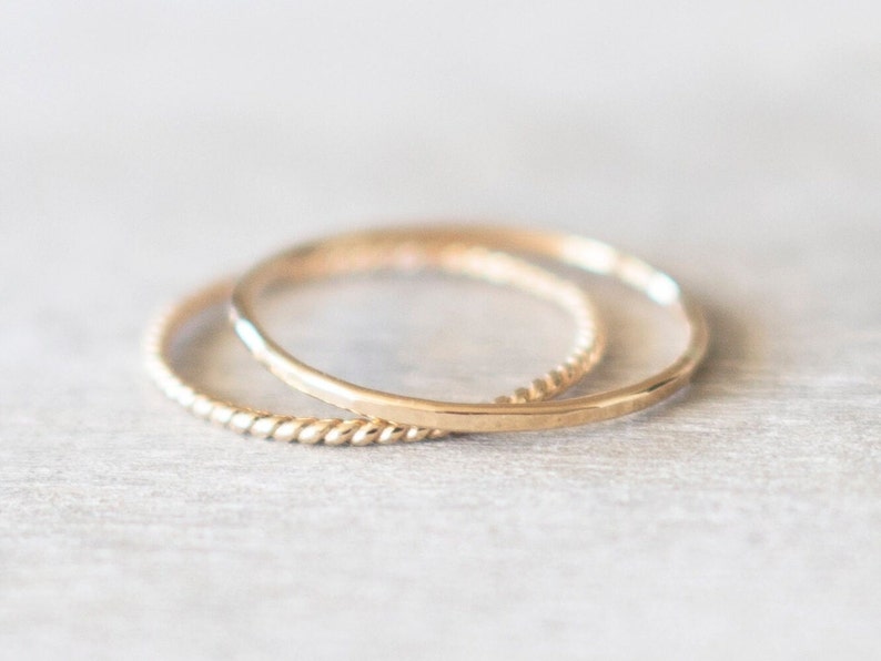 Op de afbeelding: Twee gouden ringen, een met een gladde afwerking en de andere met een gedraaid ontwerp, liggen op elkaar.