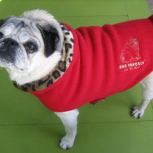 May include: A red fleece dog sweater with a leopard print trim around the neck. The sweater has a small embroidered pug wearing a hat on the back with the text "Pug Imperial" and "Est. 2012".