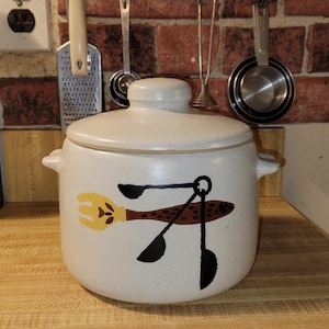 May include: White ceramic crock with a brown and black design of a fish with a fork and spoons. The crock has a lid.
