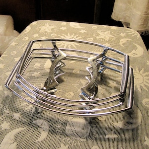 May include: A set of three chrome wire cake cooling racks. The racks are stacked on top of each other and are sitting on a white lace tablecloth.