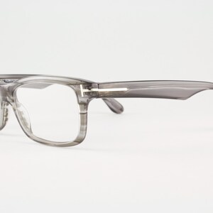 May include: Gray eyeglasses with a rectangular frame and clear lenses. The temples are a darker gray and feature a silver accent. The glasses are set against a white background.