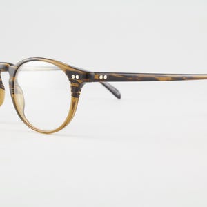 May include: Round-framed eyeglasses with a brown and tan marbled pattern. The glasses have clear lenses and small silver accents on the temples. The arms curve gently, and the overall design is classic and stylish.