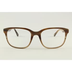 May include: A pair of eyeglasses featuring a brown and tan horizontal striped pattern on the frame. The glasses have a rectangular shape with rounded edges, a bridge, and clear lenses. The frame displays a gradient effect from darker brown at the top to a lighter tan shade at the bottom.