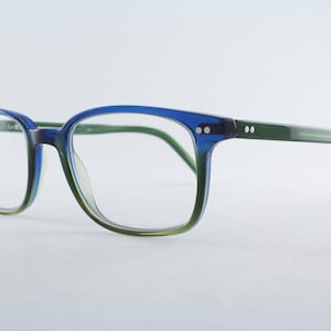 May include: Eyeglasses featuring a translucent frame that transitions from a deep blue at the top to a light green at the bottom. The temples are a solid green color, and the frame includes two small silver-toned rivets on each side of the front.