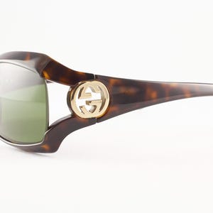 May include: Brown tortoiseshell sunglasses with a gold-tone logo on the temples. The sunglasses have a curved design and green-tinted lenses. A stylish accessory for eye protection.