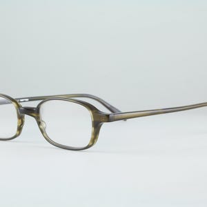 May include: A pair of eyeglasses with a translucent olive green and brown tortoiseshell patterned frame. The glasses feature oval-shaped lenses, a thin bridge, and slender temples that curve at the ends for a secure fit over the ears.