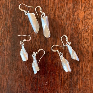 May include: Four pairs of silver earrings with a unique, twisted, and textured design. The earrings are all different lengths and have a simple hook fastening.