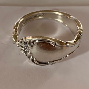 Könnte beinhalten: Ein silberner Löffelring mit floralem Design. Der Ring ist aus einem wiederverwendeten Löffel gefertigt.