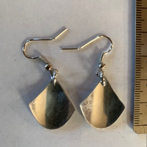 May include: A pair of silver earrings with a teardrop shape. The earrings have a simple design and are made of metal.