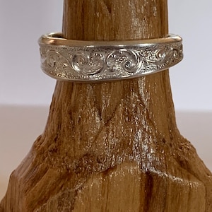 May include: A silver band ring with an intricate, engraved floral design.
