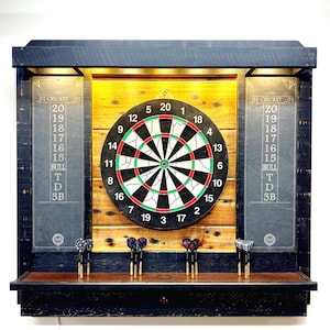 May include: A wooden dartboard cabinet with a black frame, featuring a dartboard in the center. Scoreboards are on either side. The cabinet includes a shelf with darts. The dartboard has red, green, and white accents.