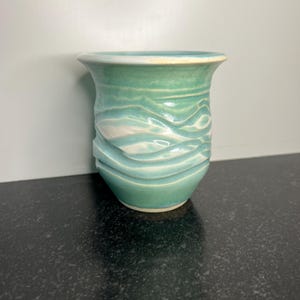 May include: A small, light blue ceramic vase with a white glaze and a wavy pattern.